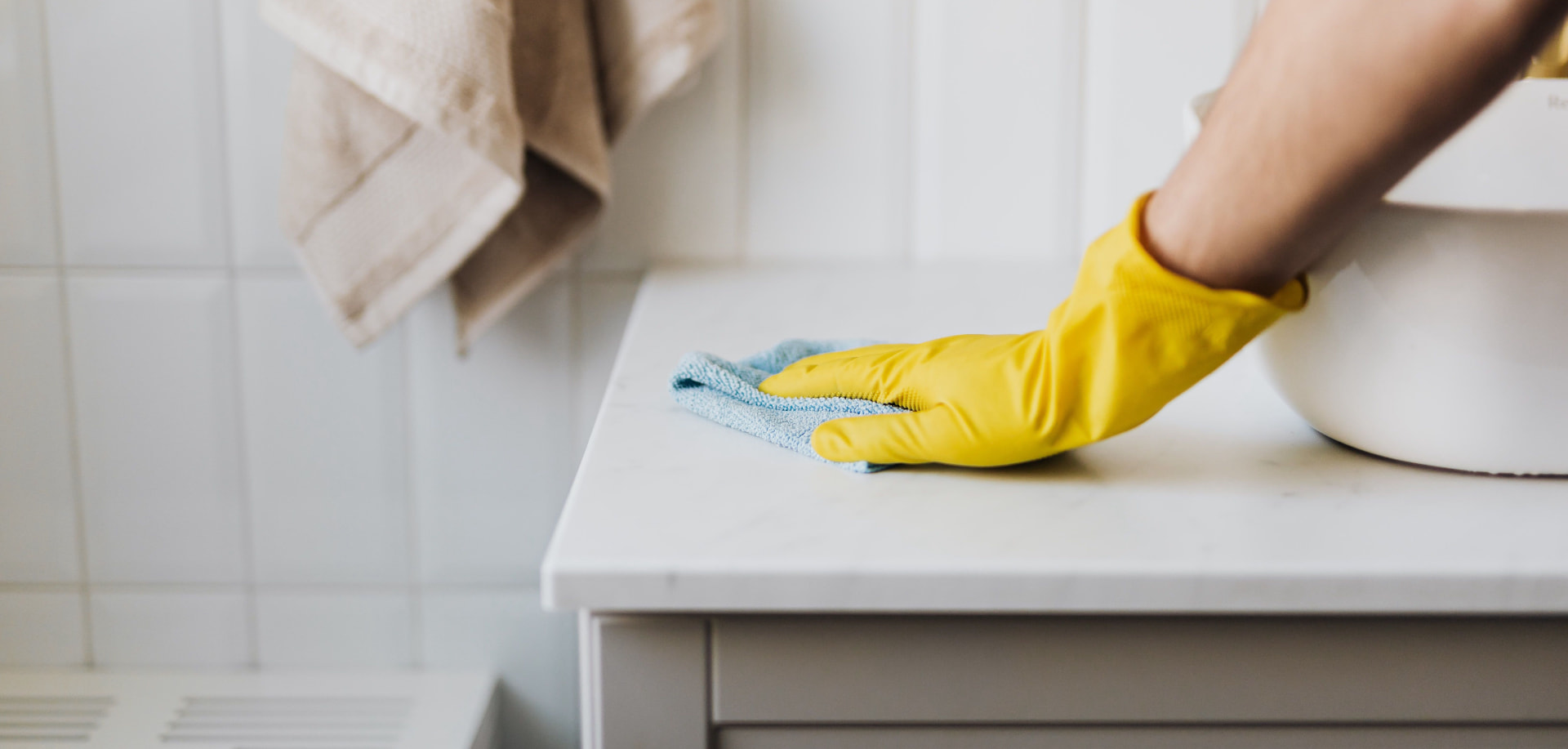 Yellow-gloved hand wiping a spotless white bathroom counter beside a white basin