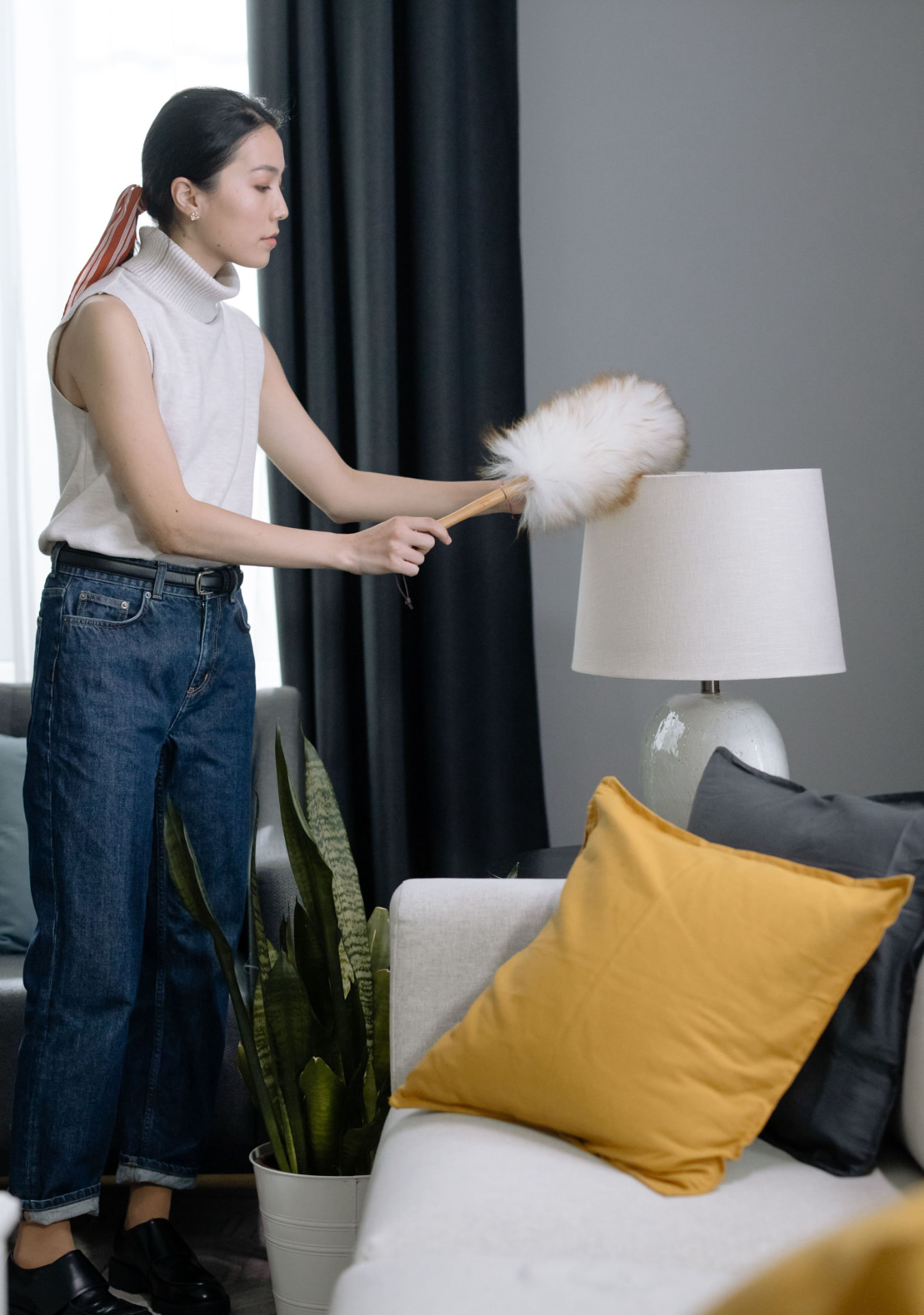 Cleaner carefully dusting a living room lamp beside a sofa