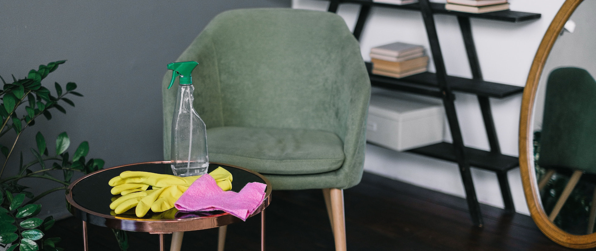 Cleaning spray bottle, yellow gloves and pink microfiber cloth arranged in a polished living room