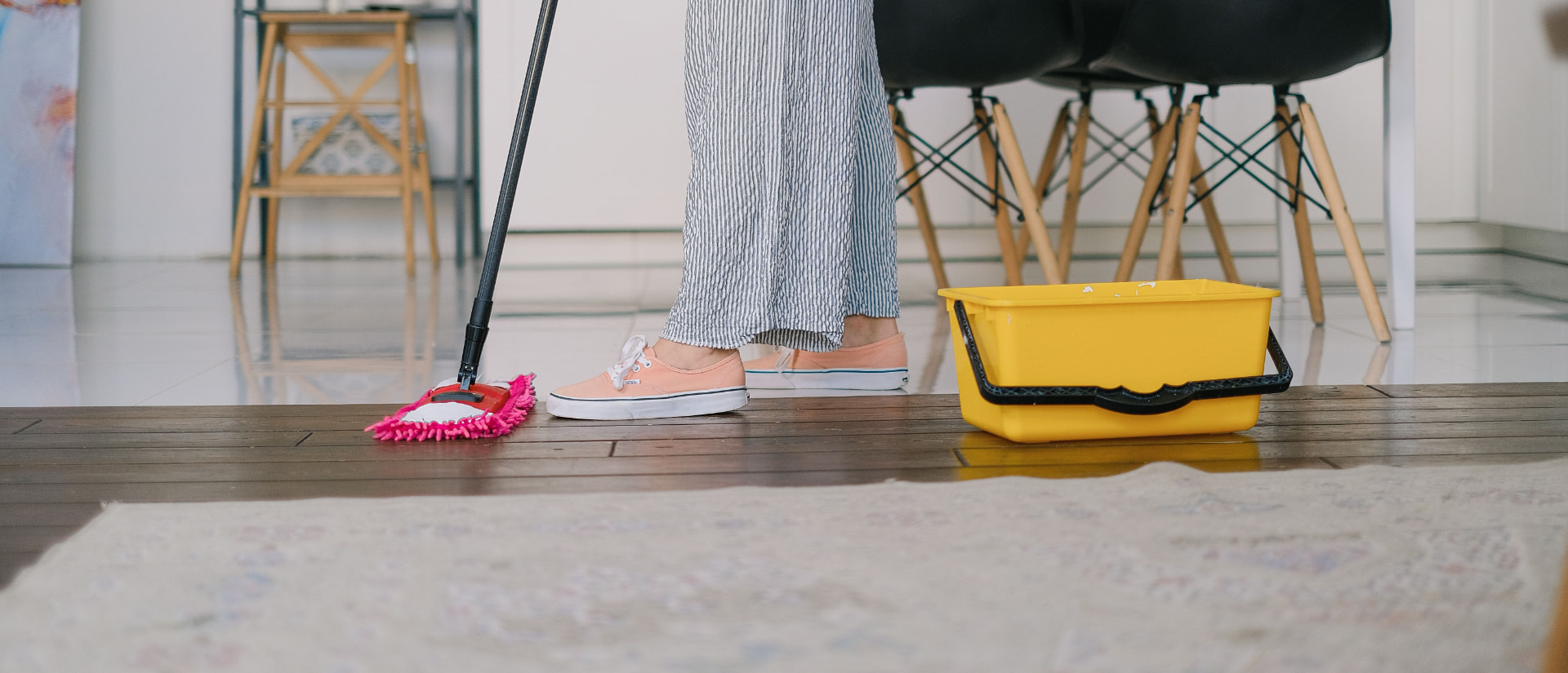 Cleaner mopping a polished wood floor beside a yellow bucket in a bright modern home